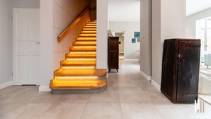 Una escalera de madera con un accesorio de luz, que conduce a una habitación con una puerta blanca y un armario de madera oscura.