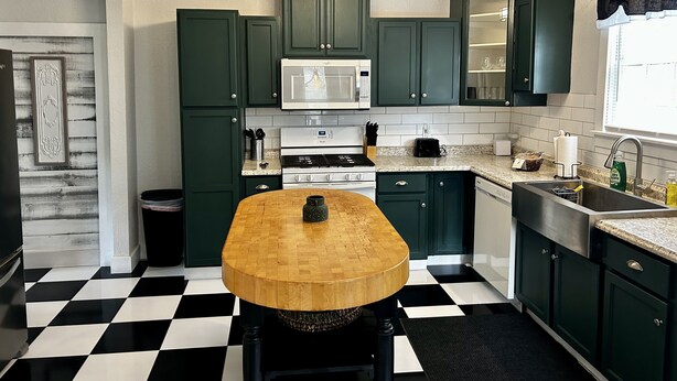 Una cocina con armarios verdes, una mesa de madera, un microondas y un fregadero.