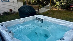 A hot tub in an outdoor setting with a hammock and a covered grill in the background.