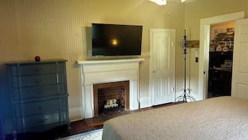 A bedroom with a bed, a dresser, a television above a fireplace, and a ceiling fan.