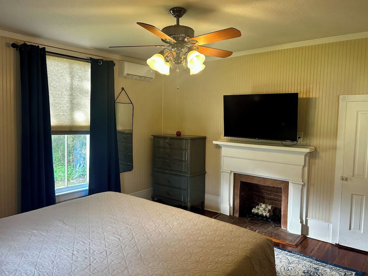 Quarto com cama, cômoda, televisão, lareira e ventilador de teto.