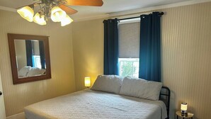 A bedroom with a bed, a bedside lamp, a nightstand, a mirror, and a window with curtains.