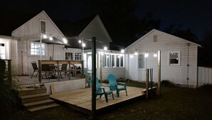 A two-story white house with a covered patio, outdoor seating, and string lights.