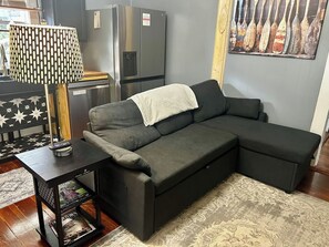 Un canapé modulable avec un plaid, une petite table avec une lampe et un réfrigérateur dans un salon.