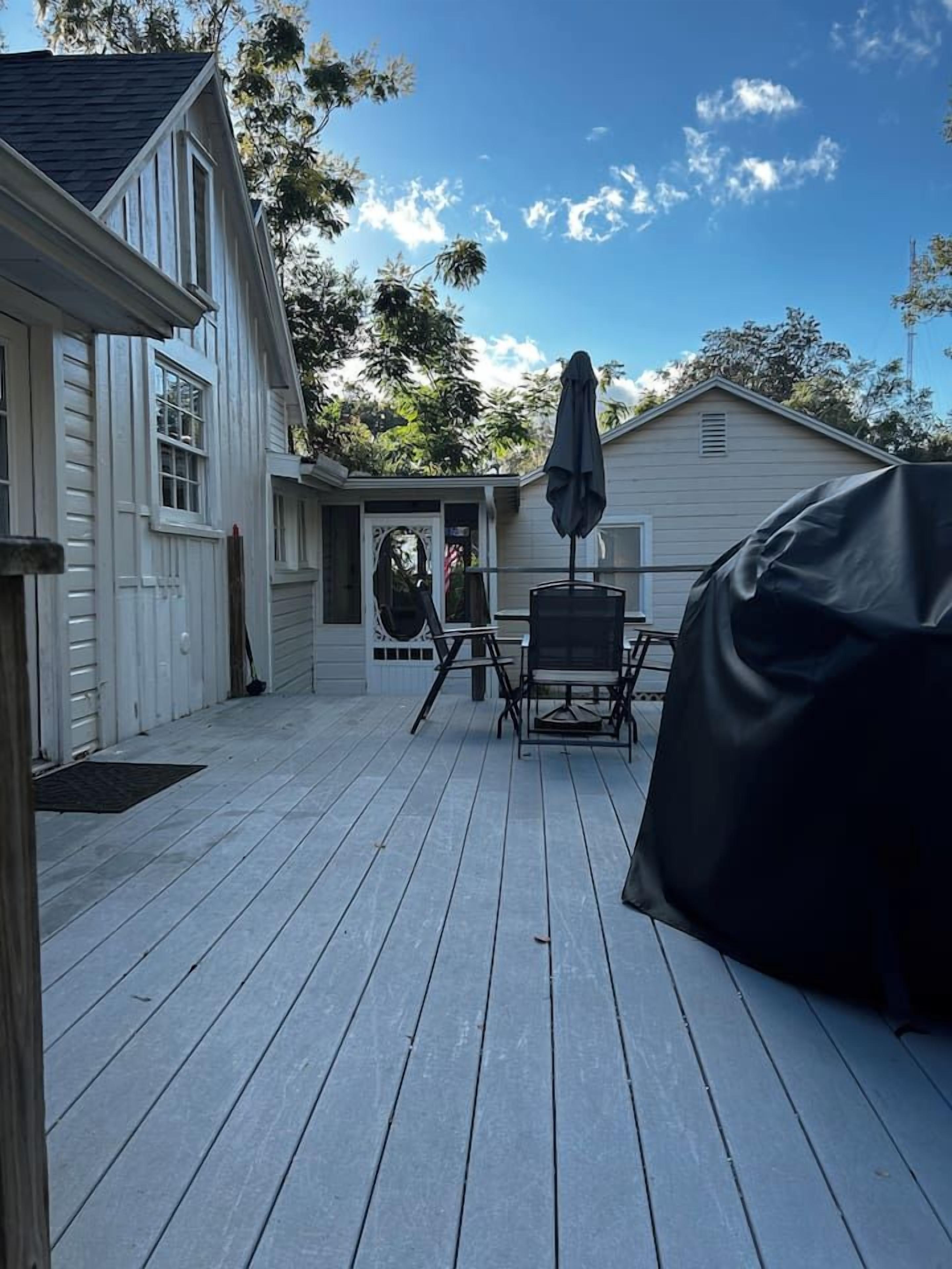 A wooden deck with a covered table and chairs, a covered grill, and a house in the background.