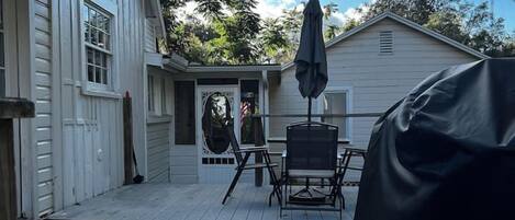 A wooden deck with a covered table and chairs, a covered grill, and a house in the background.