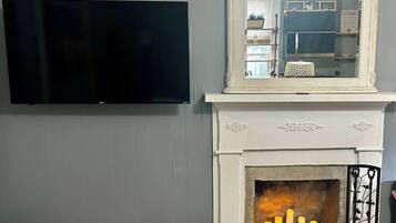 Een kamer met een wandgemonteerde flatscreen televisie, een witte haard met een spiegel erboven en een klein kandelaarhoudertje met kaarsen.