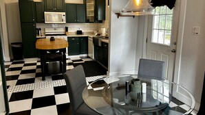 Una cocina con piso a cuadros, gabinetes verdes, un microondas y una mesa de vidrio con sillas.