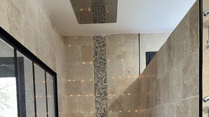 Un baño moderno con pared de mosaicos, zona de ducha y ventana con vistas a la vegetación.