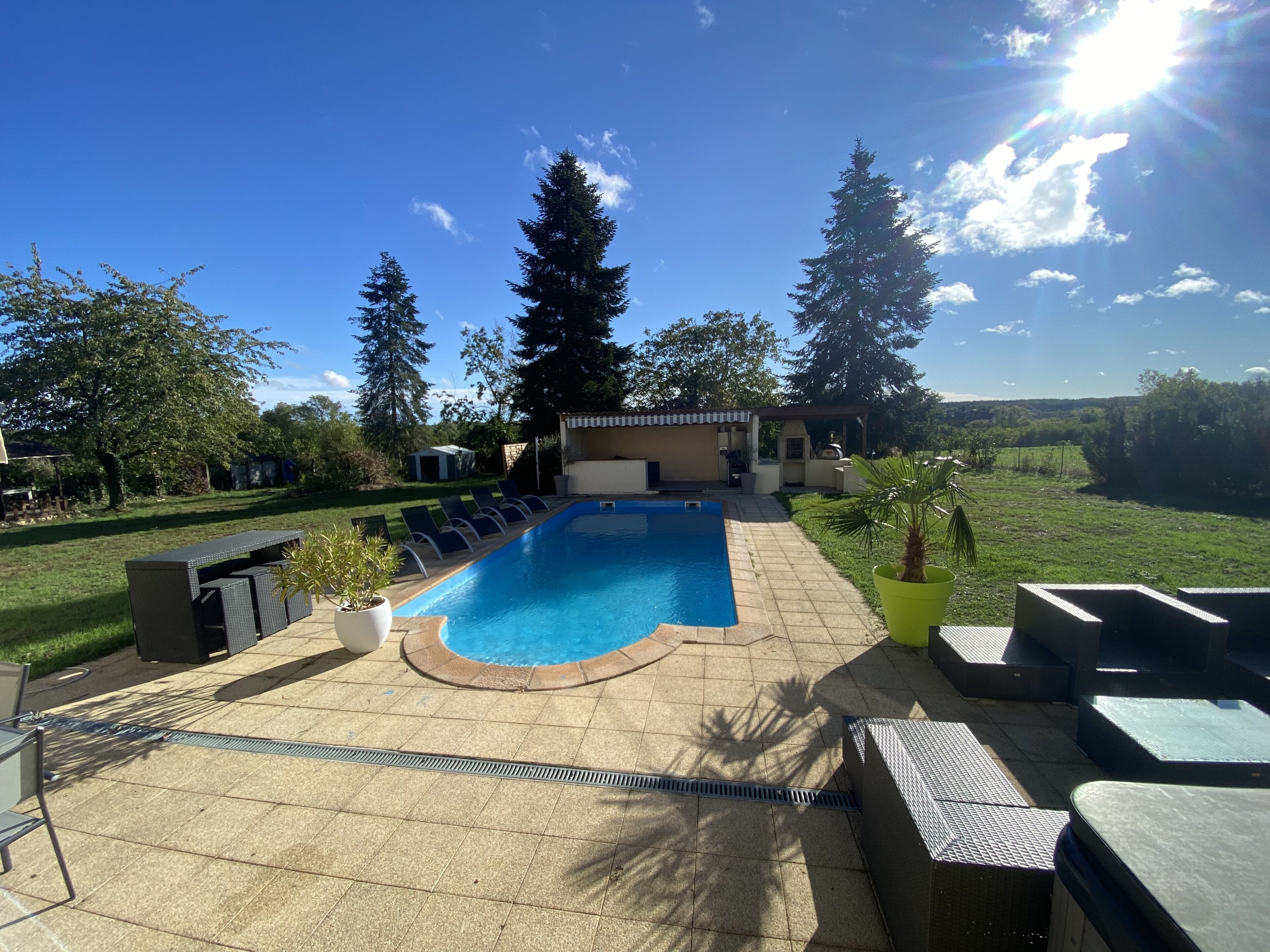 En swimmingpool med liggestole, et pergolaområde og et grillområde.