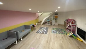 Ein geräumiges Wohnzimmer mit einem grauen Sofa, einem Spielbereich mit Spielzeug und einem Hütchenspiel, einer Treppe und einem Fernseher.