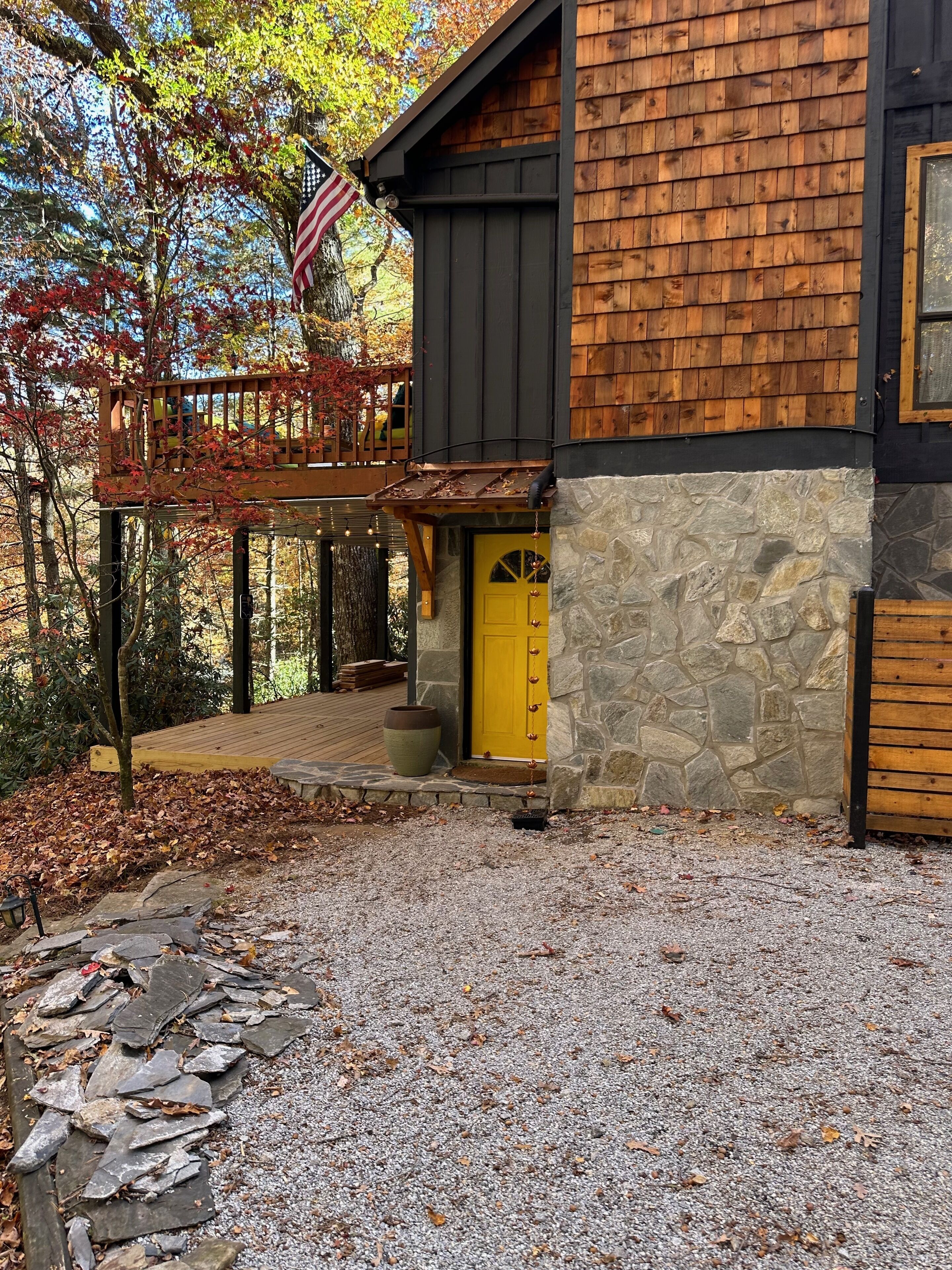A rustic cabin with a stone foundation, a wooden deck, and a yellow door.