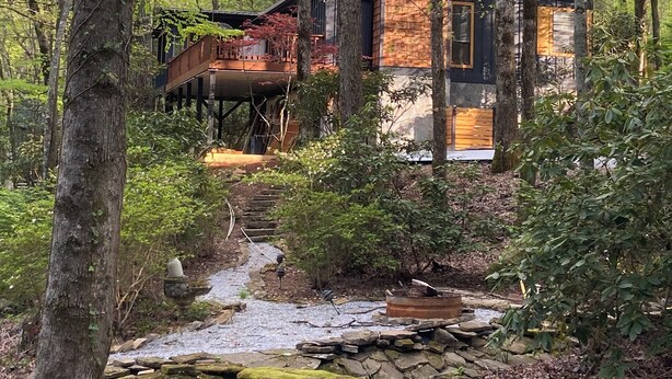 Una moderna baita di legno immersa in un bosco fitto, con un sentiero in pietra che conduce all'ingresso.