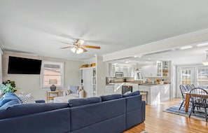 A modern living room with a dark blue sectional sofa, a dining area with a wooden table and chairs, and a kitchen with white cabinets and a central island. - 10 min to Parris Island - Pet friendly Retreat w/ Yard & 1-1 Guest House (Beaufort)