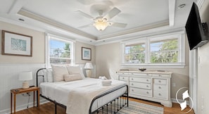 A bedroom with a bed, bedside tables, a dresser, a ceiling fan, and a TV mounted on the wall. - 10 min to Parris Island - Pet friendly Retreat w/ Yard & 1-1 Guest House (Beaufort)