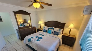 A neatly arranged bedroom with a bed, two nightstands, a ceiling fan, a mirror, and a window with blinds.