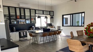 A modern kitchen with a central island, white cabinetry, and a dining area with wicker chairs and a dark rug.