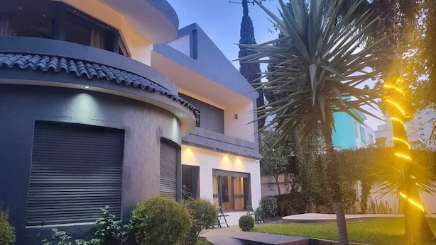 A modern house with a curved facade, a covered patio, and a well-maintained garden. - VILLA ADAM (Tangier)