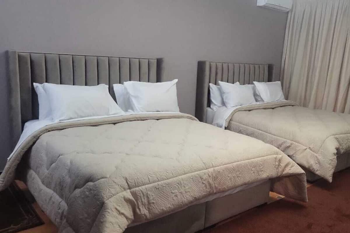 Dos camas individuales con cabeceros grises y ropa de cama blanca en una habitación de hotel.