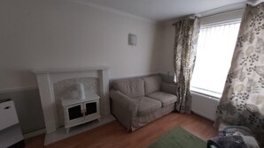 A living room with a fireplace, a sofa, and a window with curtains. - Luxurious home for long stay  (East Tilbury)