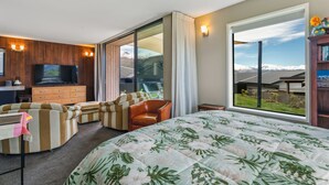 Ein modernes Hotelzimmer mit einem großen Bett, einem Fernseher, einer hölzernen Kommode und Blick auf eine Berglandschaft.