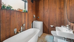 Ein Badezimmer mit Holzwänden, einer freistehenden Badewanne, einer Toilette und einem Waschbecken.
