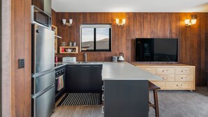 Eine moderne Küche mit Holzvertäfelung, einer großen Kochinsel, einem Einbauofen und einem Flachbildfernseher.