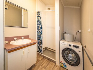 A compact bathroom with a sink, mirror, shower, and a front-loading washing machine. - Kaka Retreat - Taupo Holiday Home (Taupo)