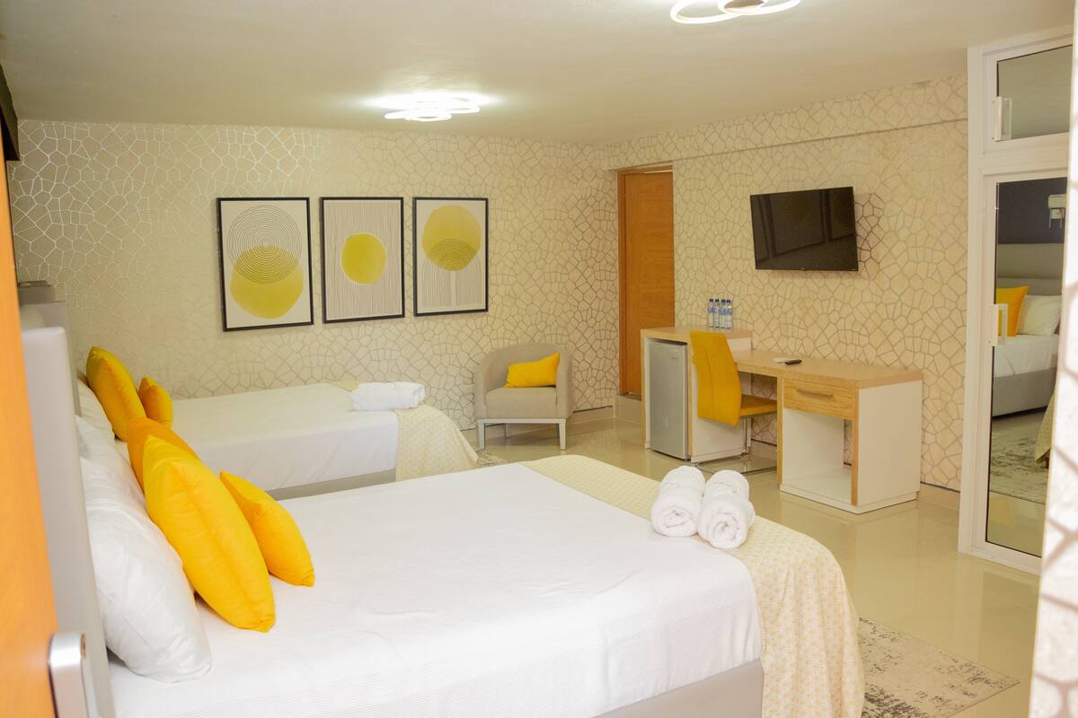 A hotel room with two beds, a desk, a chair, a TV, and artwork on the wall.
