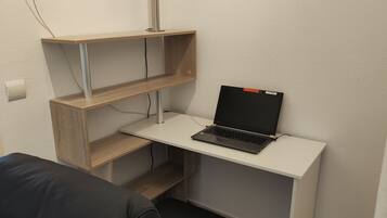 A compact workspace with a laptop on a white desk, wooden shelves, and a black chair.