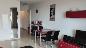 Uma sala de estar moderna com um sofá vermelho, uma mesa de jantar de vidro com cadeiras pretas, um rack vermelho com uma TV e um pôster na parede.