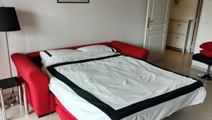 Cama bem arrumada com colcha preta e branca, cabeceira estofada vermelha e abajur de chão preto.