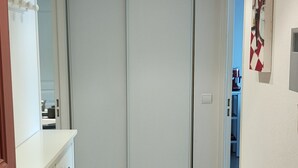 Um corredor com chão de azulejos brancos, um guarda-roupa branco e uma porta que dá para outro quarto.