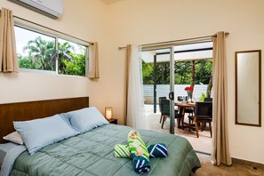 A hotel room with a bed, a nightstand, a window, and a sliding door leading to an outdoor area with a table and chairs. - Cozy 3bd private house & pool & walk to beach - Pets welcome! (Playa Negra)