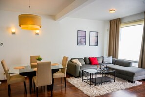 A modern living room with a glass dining table, a grey sofa, and a white shag rug.