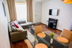 Een moderne woonkamer met een bank, een glazen salontafel en een eethoek met stoelen.