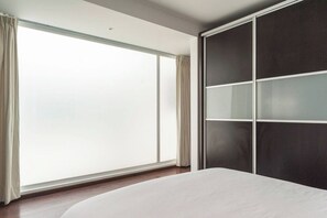 A bedroom with a large window, a bed, and a wardrobe with a sliding door.