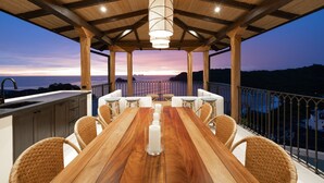 Ein Holztisch mit weißen Kerzen, Korbstühle und Blick auf das Meer im Abenddämmerung.