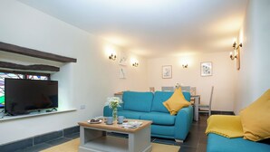 Een woonkamer met een blauwe bank, een salontafel, een televisie en wandlampen.