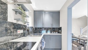 Une cuisine moderne avec des plans de travail en marbre, des meubles gris et un four encastré.
