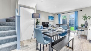 Un espace de repas moderne avec une table dressée pour quatre personnes, un escalier et une vue sur l’extérieur.