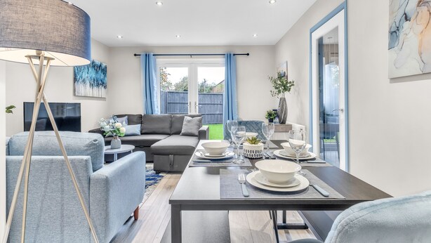 Un salon moderne avec un coin repas, des canapés gris, un grand lampadaire et une vue sur l’extérieur.