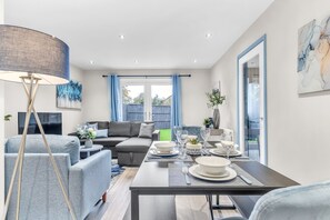En moderne stue med spiseplads, grå sofaer, en stor gulvlampe og udsigt til det fri.