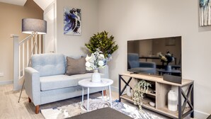 Un salon moderne avec un canapé gris, une table basse ronde blanche, un téléviseur posé sur un meuble en bois et une lampe sur pied.