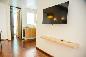 Un interior moderno con piso de madera, una zona de cocina y un televisor de pantalla plana montado en la pared.