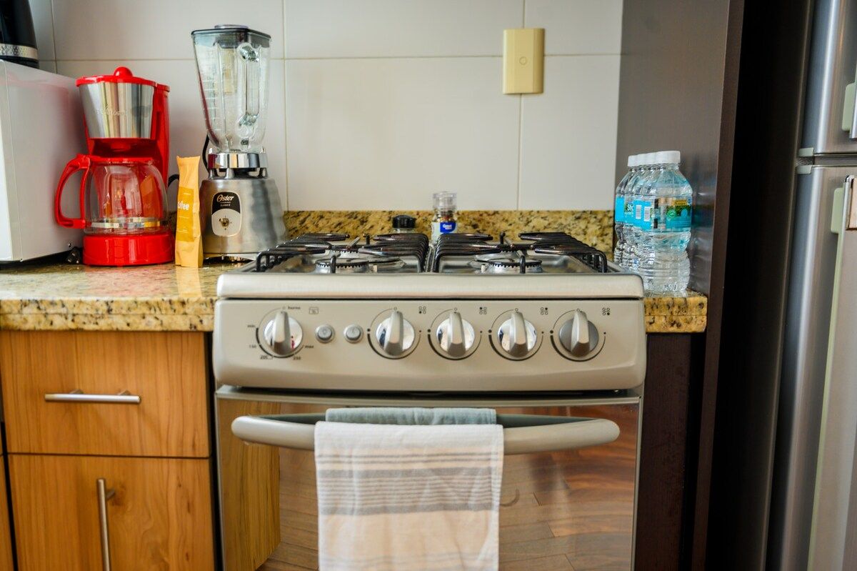 A kitchen with a gas stove, a coffee maker, a blender, and a water bottle.
