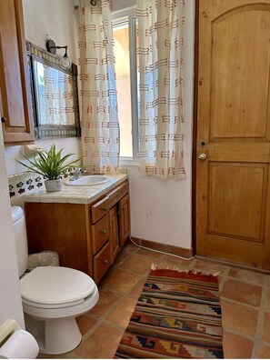 Bathroom features a toilet, sink, and decorative mirror, with patterned curtains and a rug.