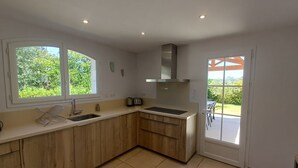 A modern kitchen with wooden cabinets, a sink, a stove, and a window overlooking greenery. - La Bastide Saint Roch - Modern and spacious in a quiet location with a pool (La Tour-d'Aigues)