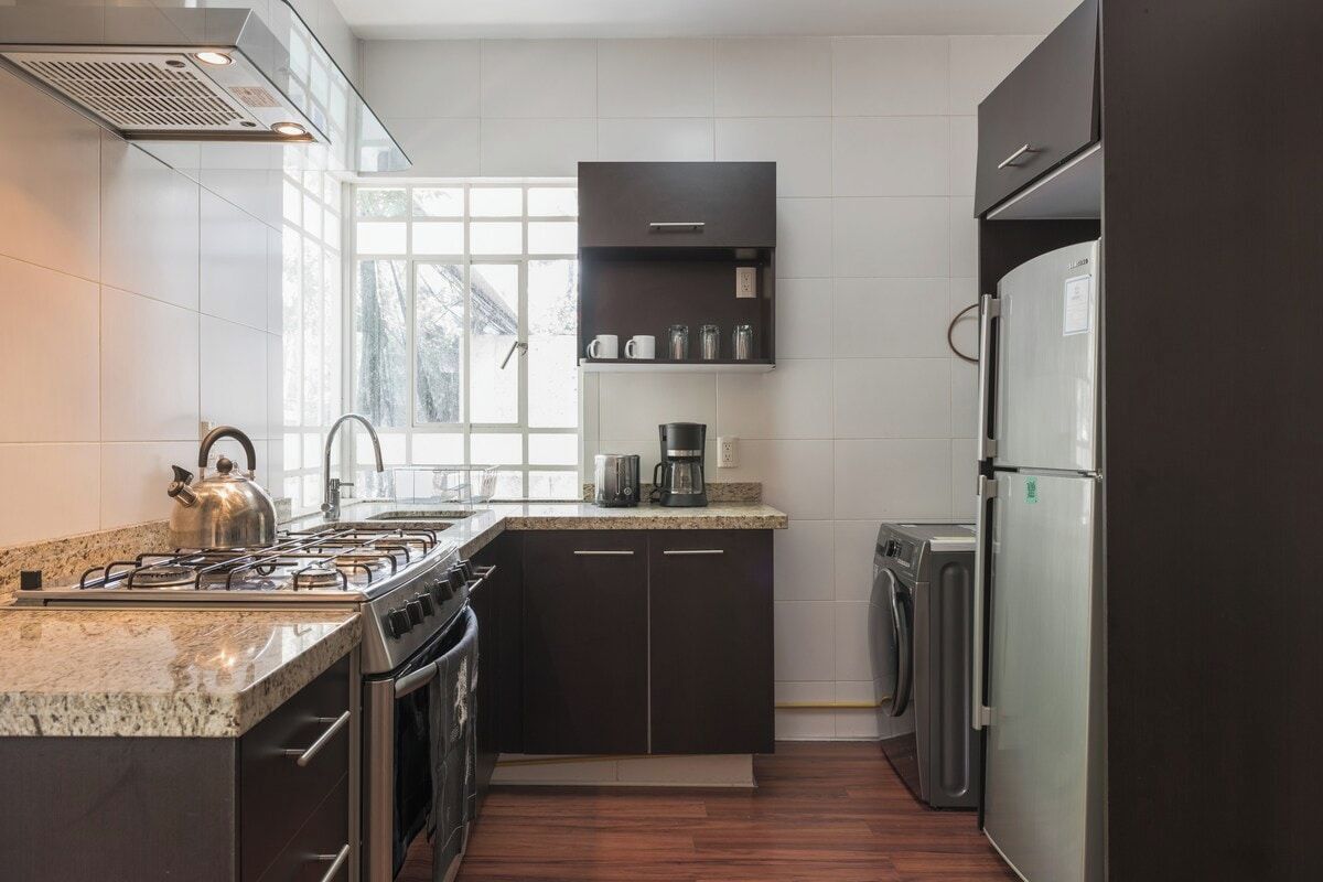Une cuisine moderne équipée d’une cuisinière à gaz, d’un four, de meubles de rangement de couleur sombre, d’un réfrigérateur en acier inoxydable et d’une machine à café.