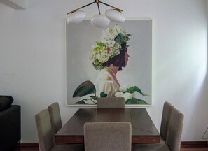 A dining area with a table and chairs, a framed artwork on the wall, and a ceiling light fixture.